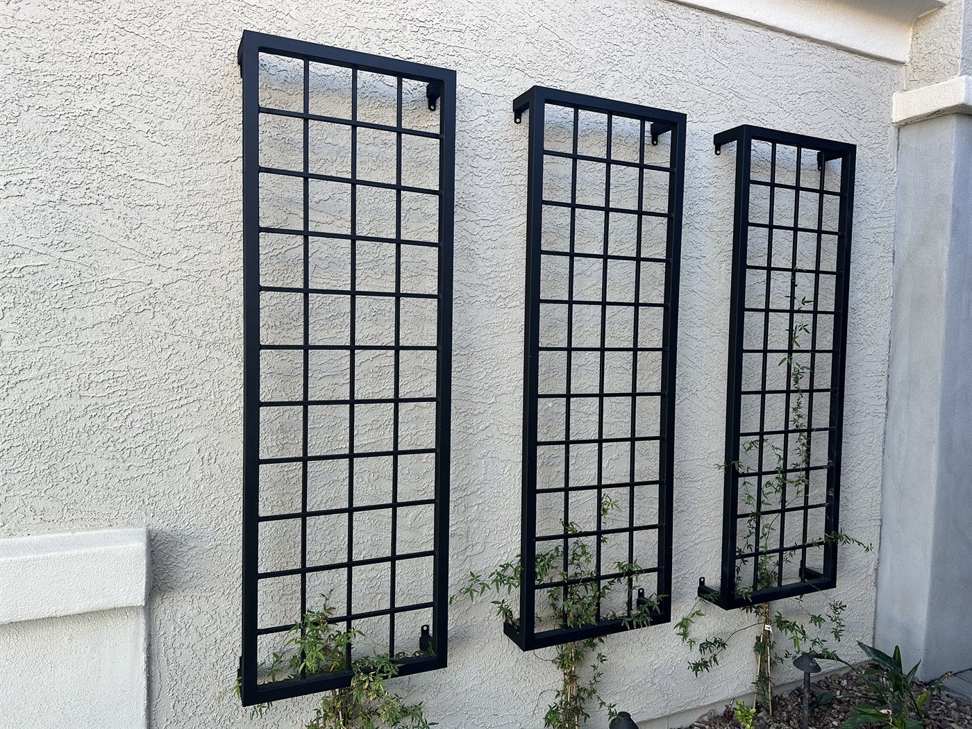 Three matching window-grid steel trellis panels on a stucco wall